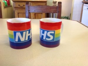 A picture of two coffee mugs with rainbow colours and NHS on side