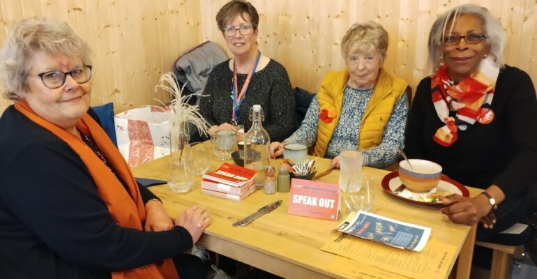 Four SI Glasgow City members sitting at a table at a cafe with 'speak out' table tents on the table.