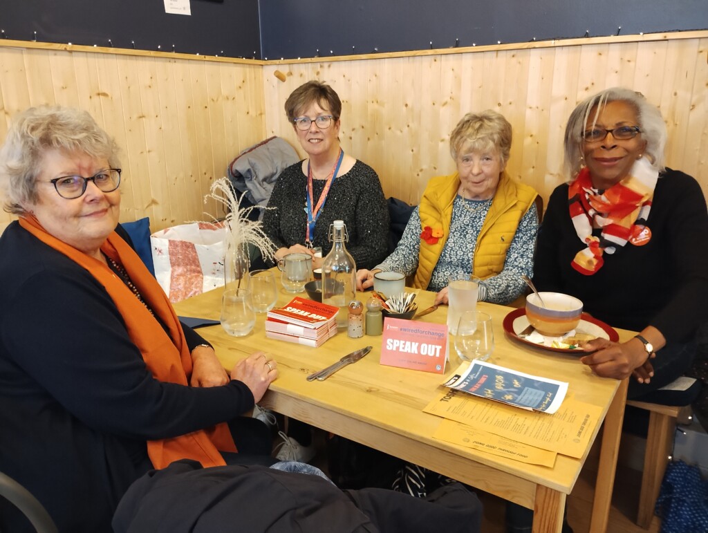 Four SI Glasgow City members sitting at a table at a cafe with 'speak out' table tents on the table.