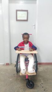 Malawian boy with legs in plaster ina wheelchair with tray