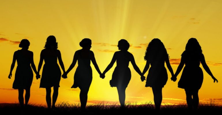 Women walking into the sunset holding hands
