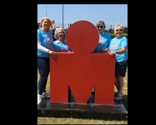 Photo of four women in blue T shirts posing with the red Ironman Logo