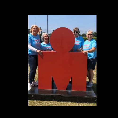 Photo of four women in blue T shirts posing with the red Ironman Logo