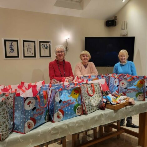 Gillian, Valerie and Jackie with 25 brightly coloured Christmas gift bags on a table
