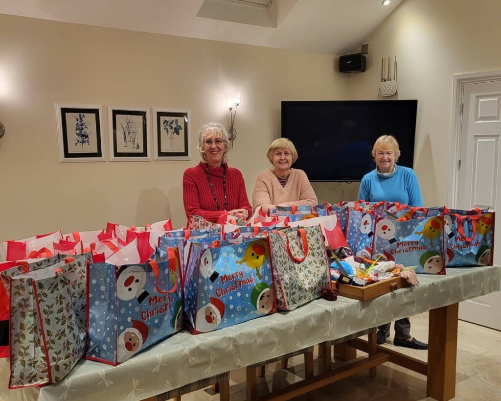 Gillian, Valerie and Jackie with 25 brightly coloured Christmas gift bags on a table