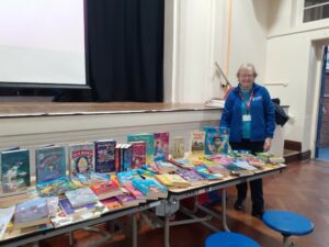 Club Secretary Jackie stands at the side of a table filled with books