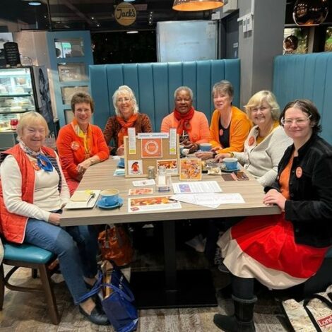Members of Swindon Soroptimists sitting around a cafe table, all in orange