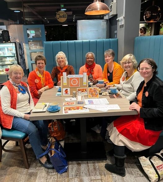 Members of Swindon Soroptimists sitting around a cafe table, all in orange