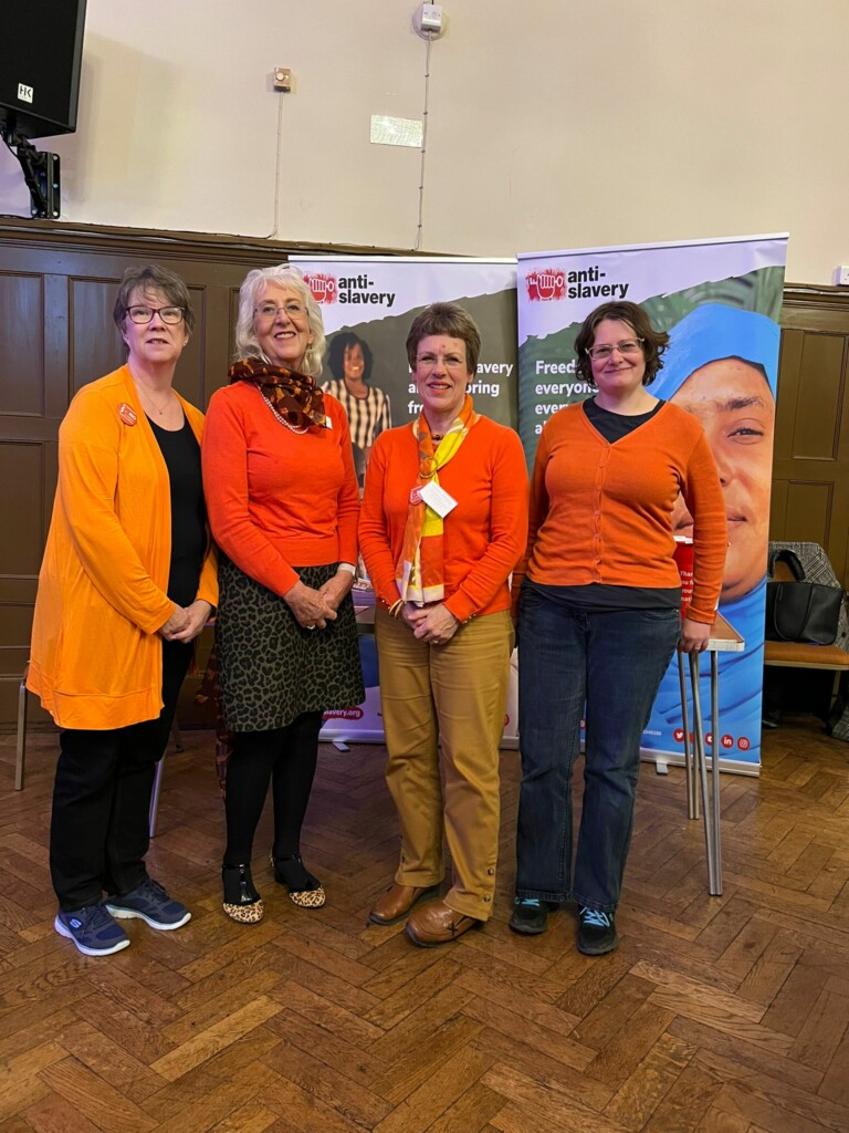 Members of Swindon Soroptimists wearing orange, while standing next to a display for Anti-Slavery International